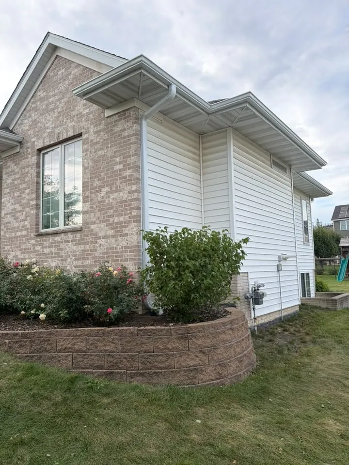 Corner of a brick and white siding home above a block retaining wall