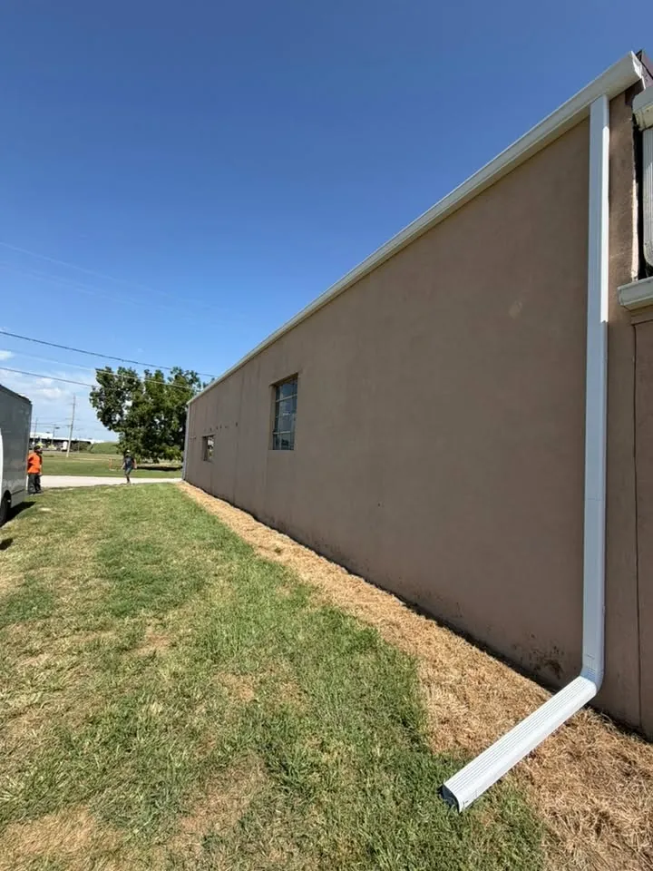 Tan commercial building wall with a gutter and long downspout to the grass