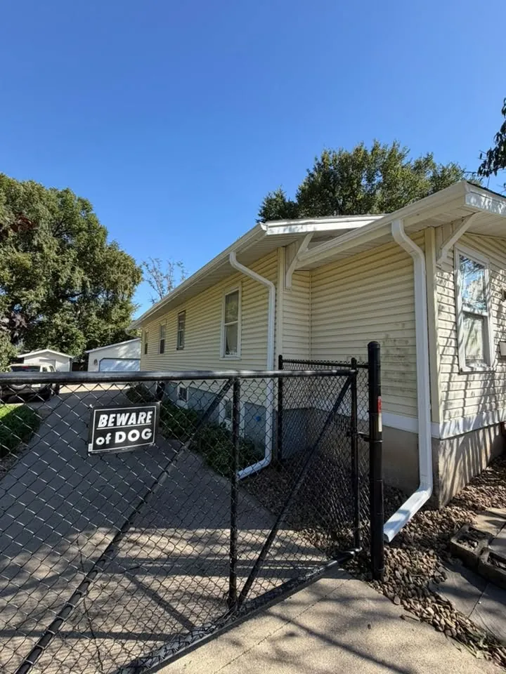 White gutters and downspout on a cream house beside a chain link fence