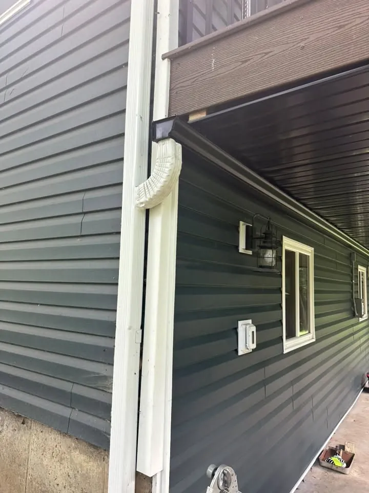 White downspout running down dark gray-green siding