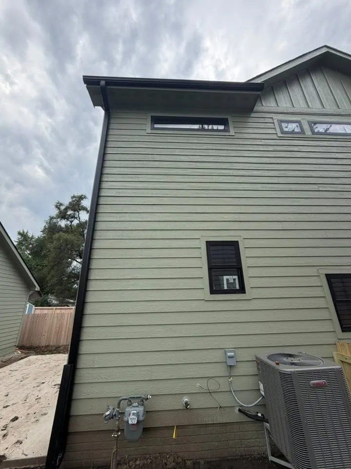 Sage green board siding with a black gutter and downspout by an air conditioner