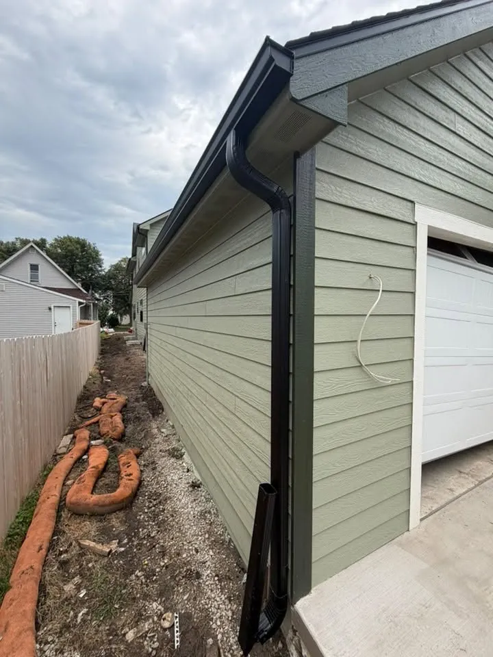 New sage green siding with black gutters and downspouts beside a garage
