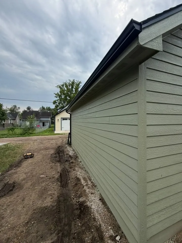 Side of a new build in sage green siding with fresh dirt and a black gutter