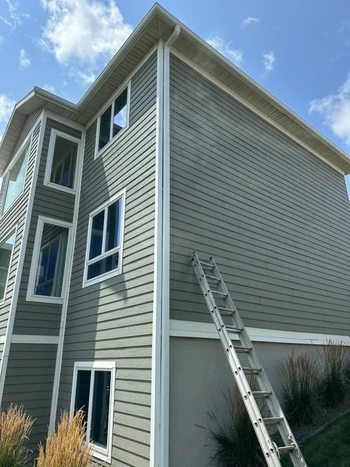 Tall sage green sided wall with white trim and a ladder against it