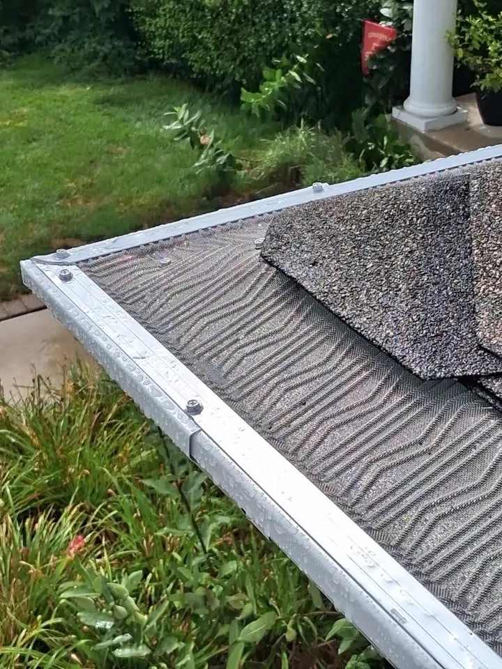 White gutter with a leaf guard screwed down at the corner of a shingled roof