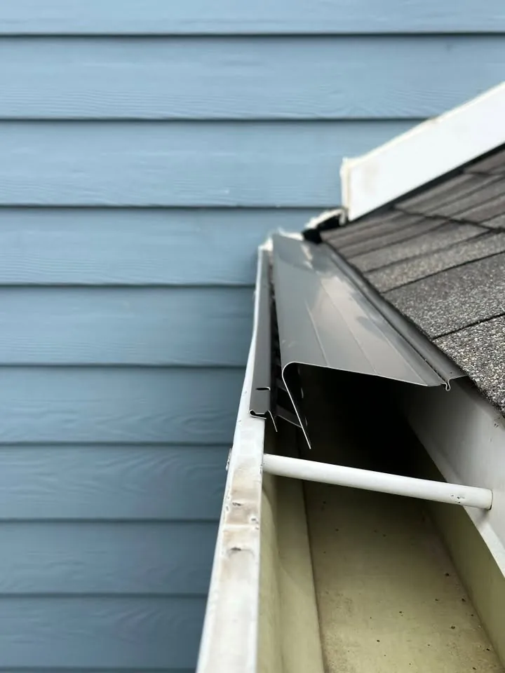 Inside of a new gutter showing a hidden hanger against blue siding