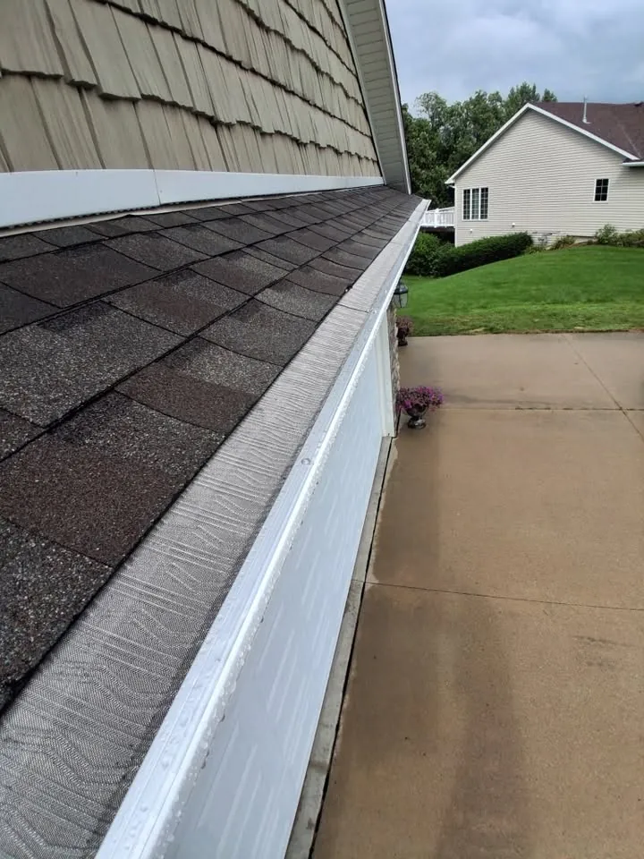 White gutter run along a roof edge above shake siding and a driveway