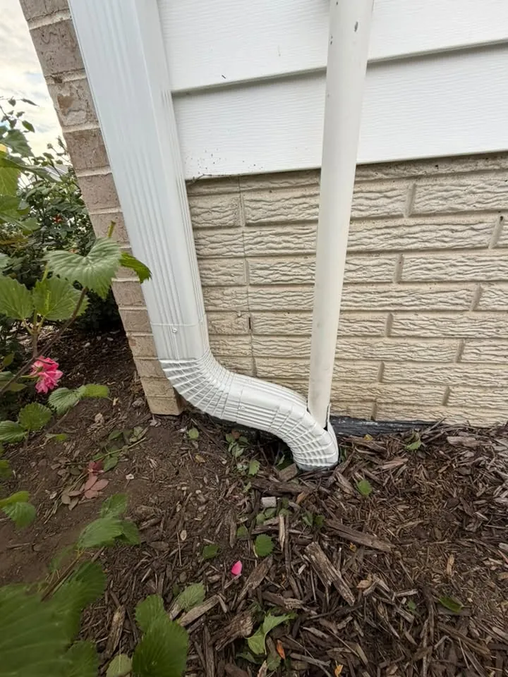White downspout with an elbow turning out over a mulch flower bed