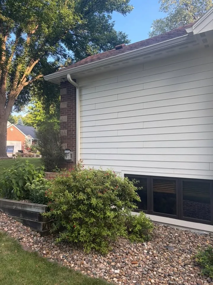 White siding and brick home with gutters above a landscaped bed