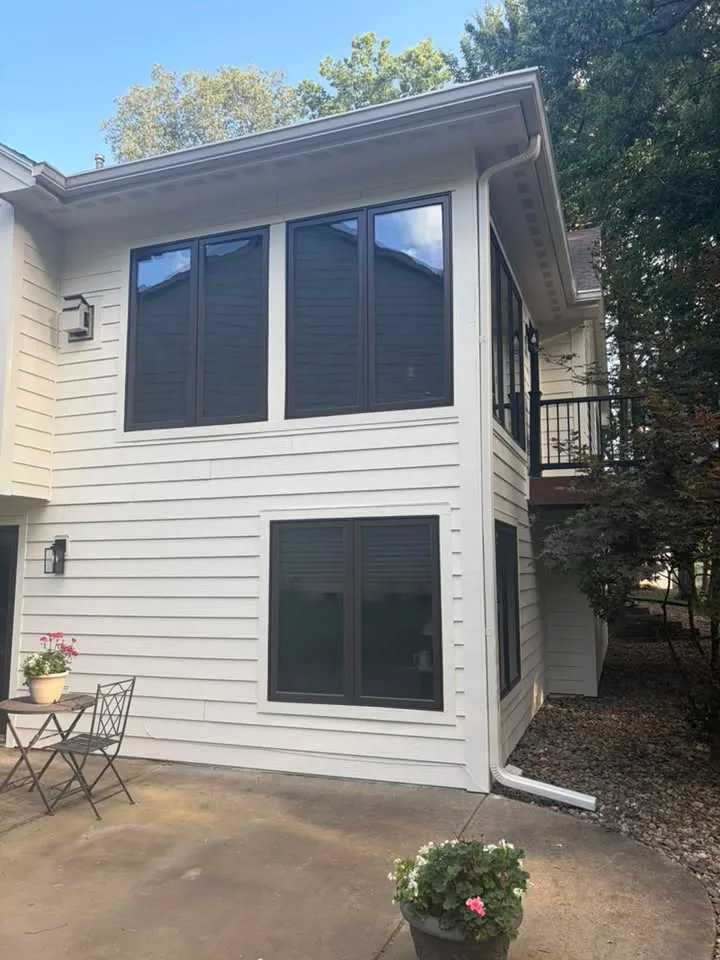 Two-story white sided home with large dark-framed windows above a patio