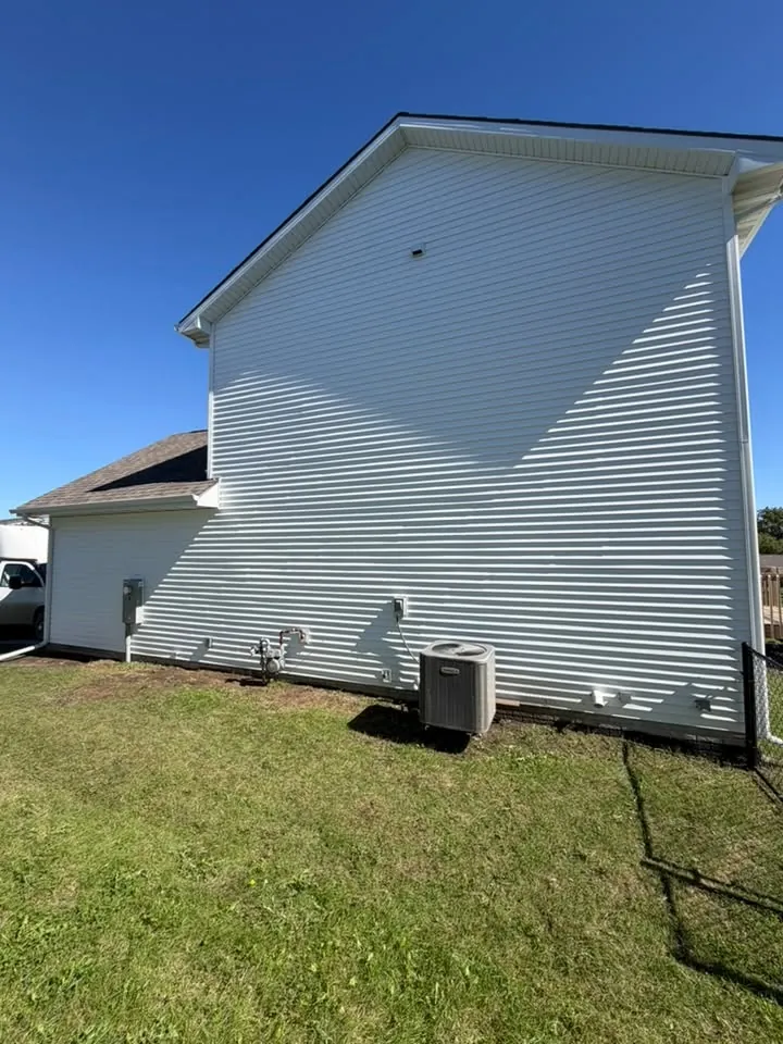 Tall gable wall finished in new white vinyl siding under a clear sky